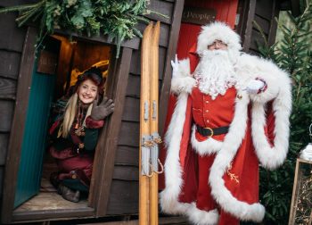 Father Christmas and an elf outside a cabin