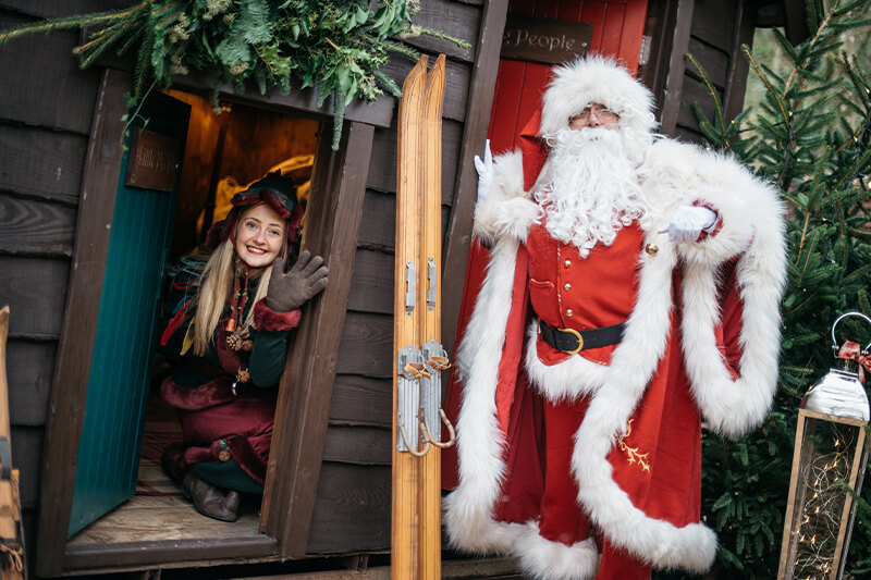 Father Christmas and an elf outside a cabin