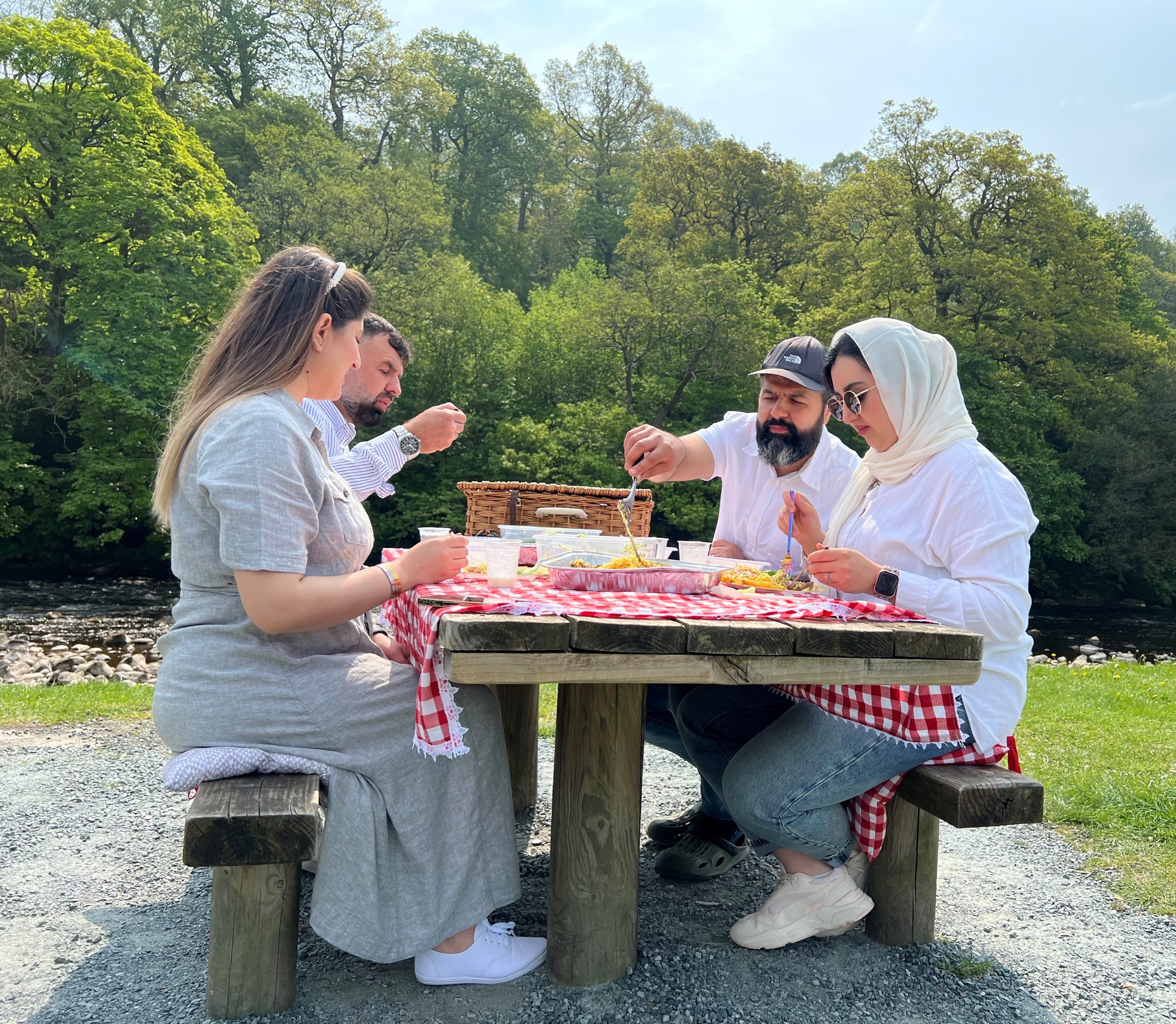 Family sat at a picnic table by the River Wharfe near Bolton Abbey