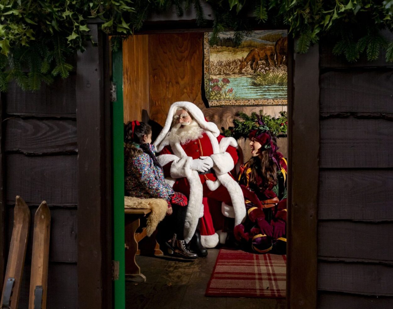 Little girl sits down with Father Christmas for a chat near the entrance to his log cabin