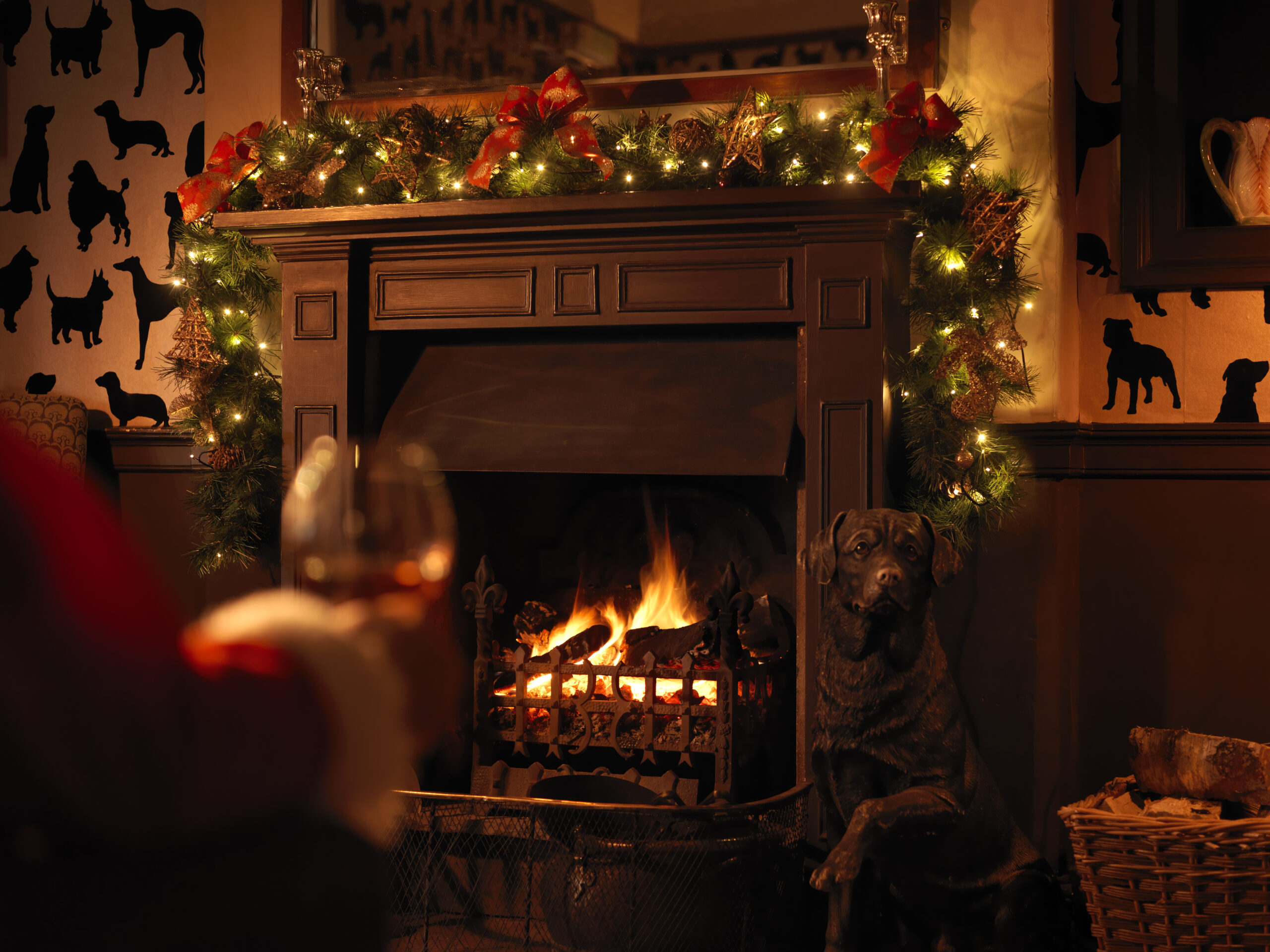 an inviting log fire burning under the large dark brown wooden mantelpiece at the Devonshire Arms, with green winter foliage and fairy lights surrounding it